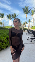 Mujer con vestido de malla transparente negro de manga larga sobre bikini, frente a palmeras